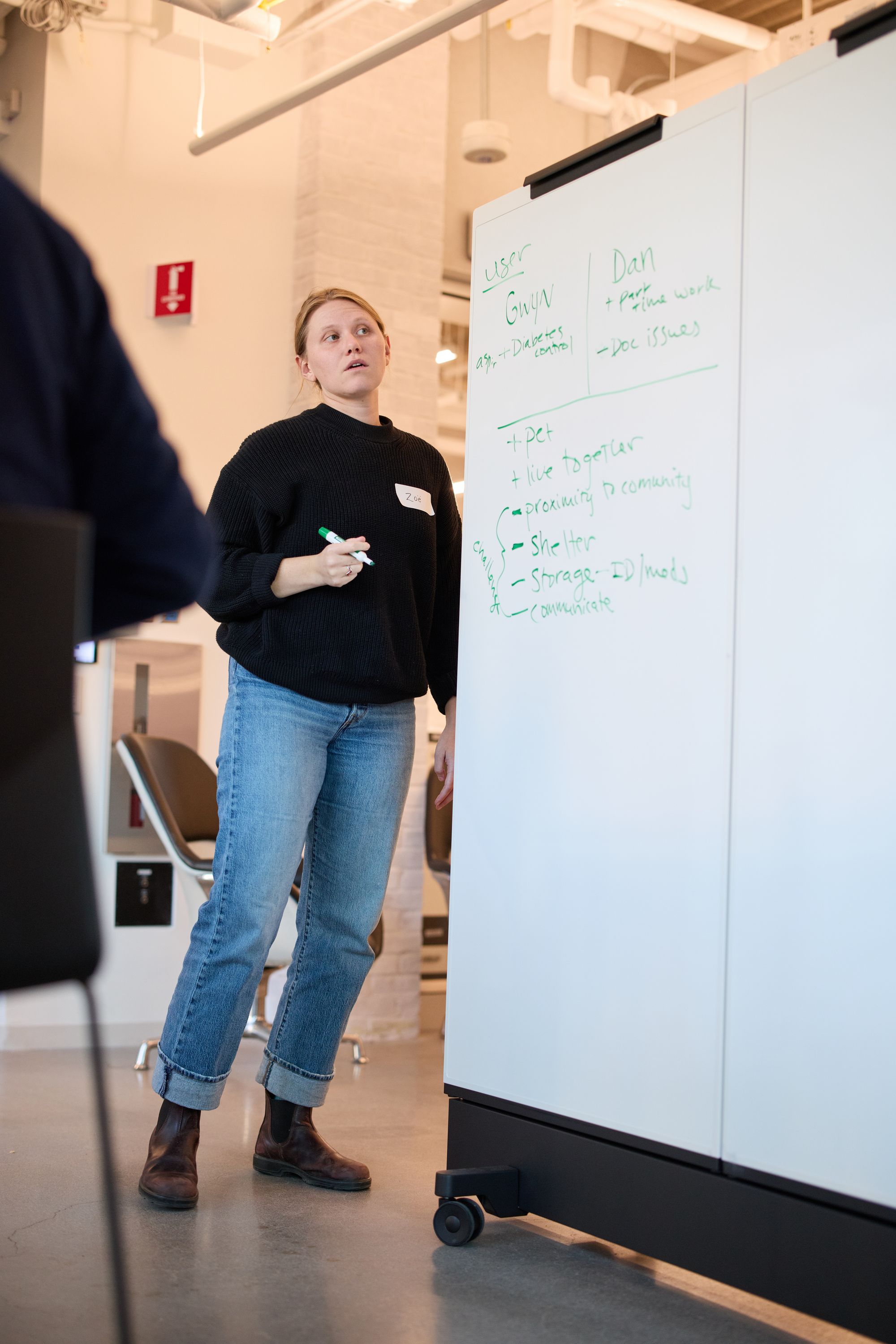 An attendee stands beside her group's whiteboard, looking at their breakdown of user needs.